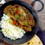 Portrait overhead image of an onion rich beef dopiaza curry served in an iron karahi with rice and a coriander garnish