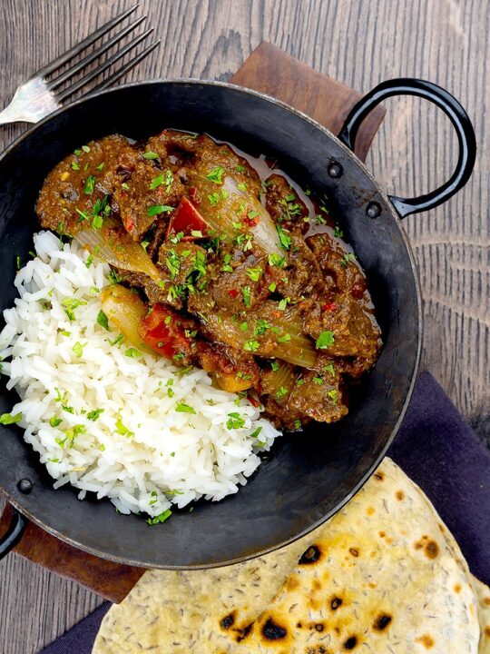 Portrait overhead image of an onion rich beef dopiaza curry served in an iron karahi with rice and a coriander garnish