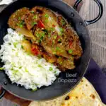 Portrait overhead image of an onion rich beef dopiaza curry served in an iron karahi with rice and a coriander garnish with a text overlay