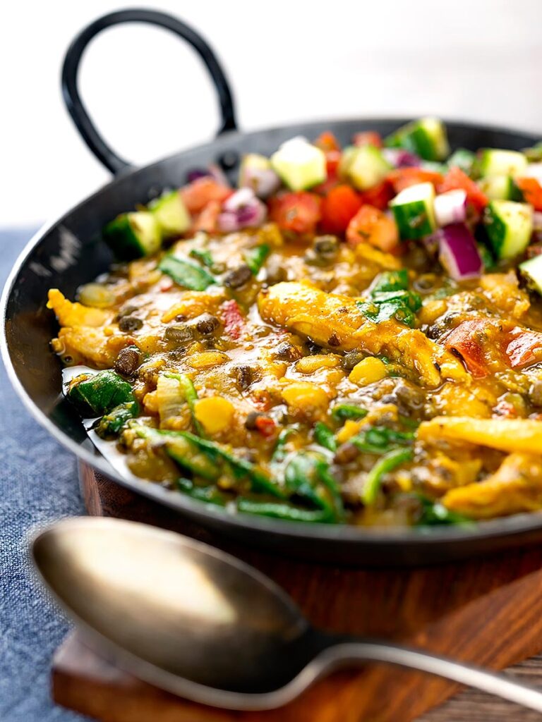 Portrait image of an Indian Chicken Dhansak lentil curry served in a cast iron karahi with a kachumber salad
