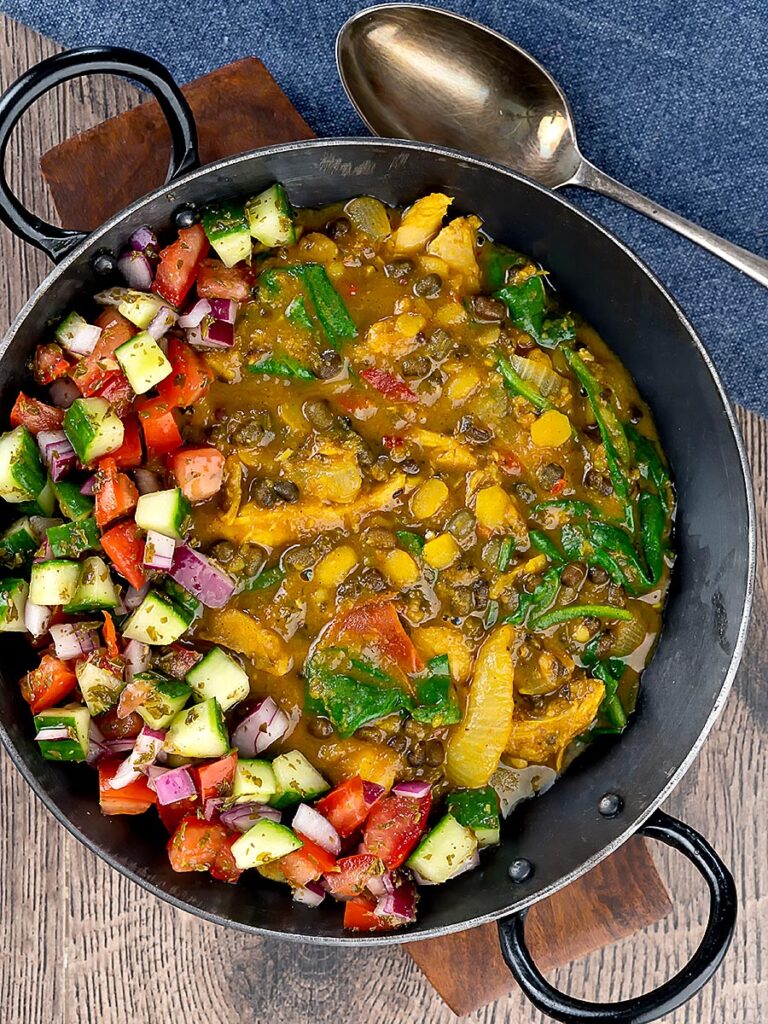 Portrait overhead image of an Indian Chicken Dhansak lentil curry served in a cast iron karahi with a kachumber salad