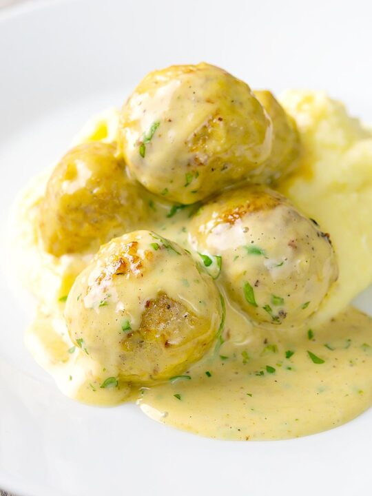 Portrait image of chicken meatballs in a creamy honey and mustard sauce with text overlay served with mashed potato