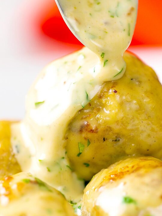 Portrait image of chicken meatballs having a creamy honey and mustard sauce poured over them