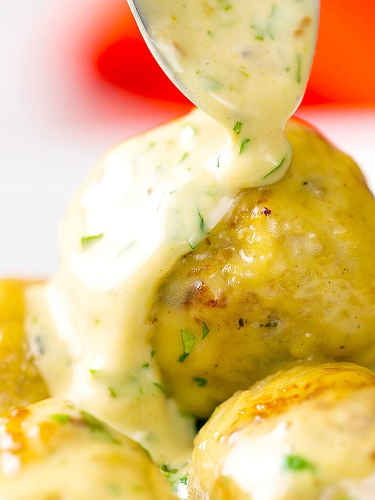 Portrait image of chicken meatballs having a creamy honey and mustard sauce poured over them