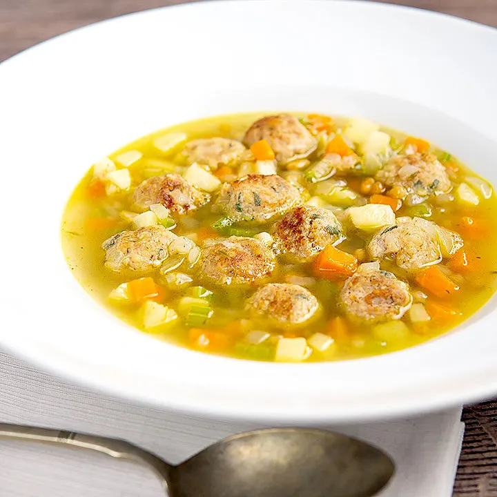 Square image of an simple pork meatball soup in a golden vegetable broth served in a white bowl