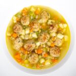 Portrait overhead image of an simple pork meatball soup in a golden vegetable broth served in a white bowl