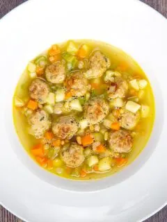 Portrait overhead image of an simple pork meatball soup in a golden vegetable broth served in a white bowl