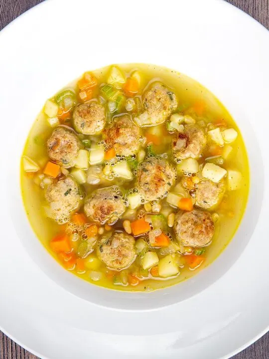 Portrait overhead image of an simple pork meatball soup in a golden vegetable broth served in a white bowl