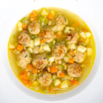 Portrait overhead image of an simple pork meatball soup in a golden vegetable broth served in a white bowl with a text overlay
