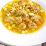 Portrait image of an simple pork meatball soup in a golden vegetable broth served in a white bowl