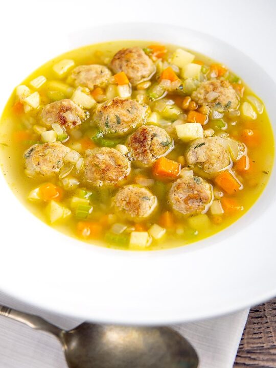 Portrait image of an simple pork meatball soup in a golden vegetable broth served in a white bowl