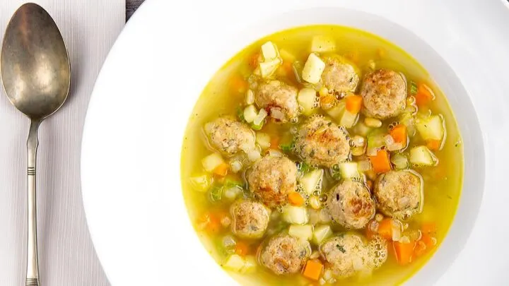 Landscape overhead image of an simple pork meatball soup in a golden vegetable broth served in a white bowl