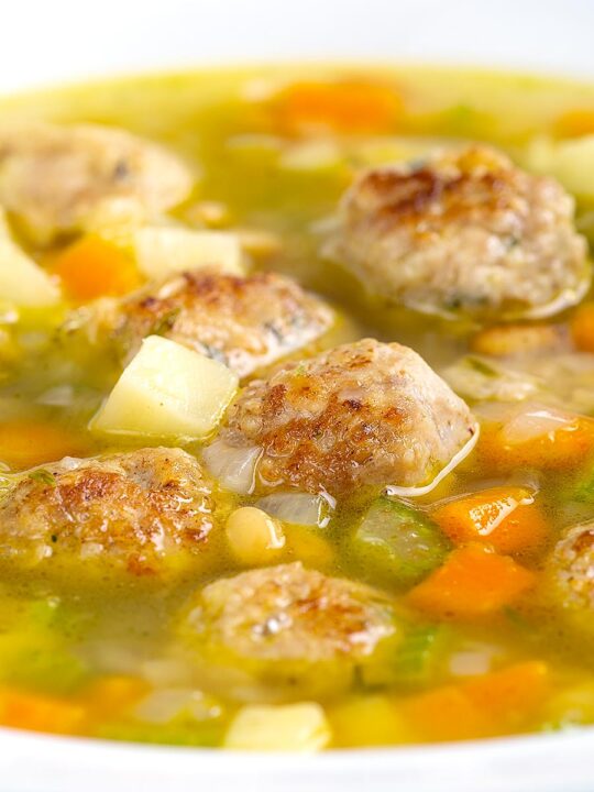 Portrait close up image of an simple pork meatball soup in a golden vegetable broth served in a white bowl