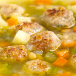 Portrait close up image of an simple pork meatball soup in a golden vegetable broth served in a white bowl with a text overlay