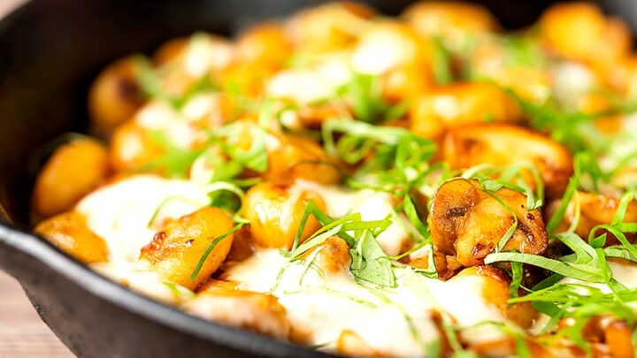 Landscape image of baked gnocchi with mushrooms in balsamic vinegar, mozzarella cheese and fresh basil served in a cast iron skillet