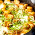 Portrait image of baked gnocchi with mushrooms in balsamic vinegar, mozzarella cheese and fresh basil served in a cast iron skillet with a text overlay