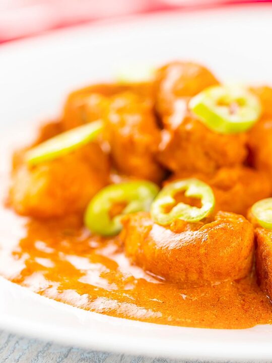 Portrait image of a Hungarian fish paprikash or harcsapaprikash served on a white plate in a silky paprika rich sauce