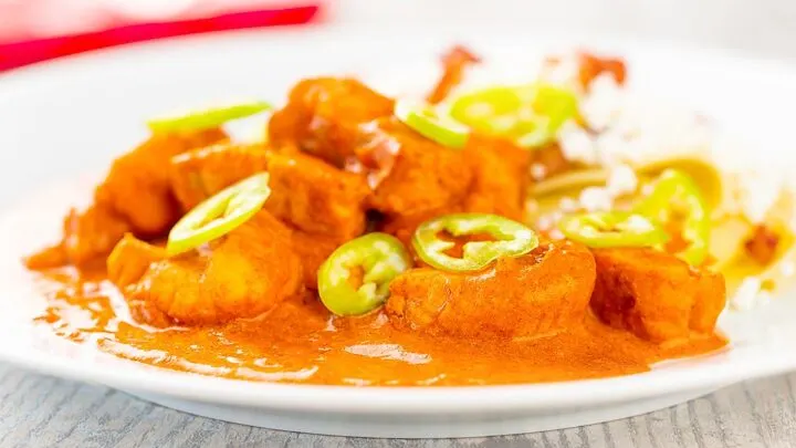 Landscape image of a Hungarian fish paprikash or harcsapaprikas served on a white plate in a silky paprika rich sauce