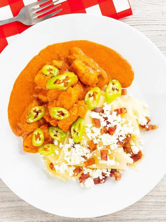 Portrait overhead image of a Hungarian fish paprikash or harcsapaprikash served on a white plate in a silky paprika rich sauce