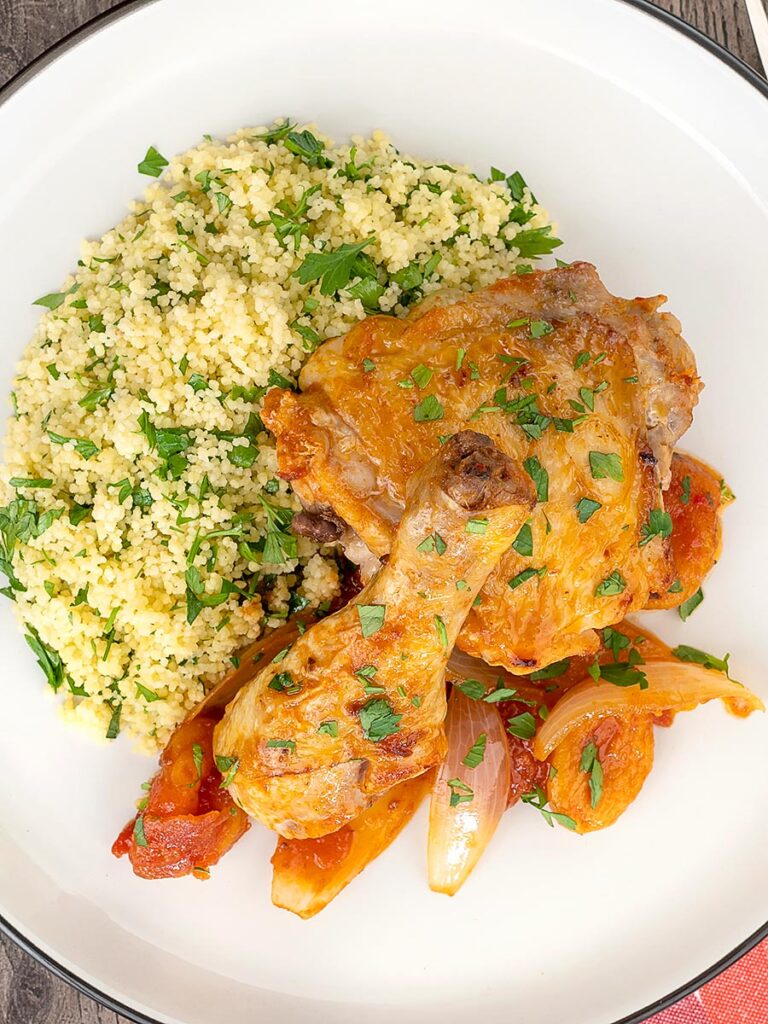 Portrait overhead image of a Moroccan influenced chicken tagine with dried apricots made with chicken drumsticks and thighs served with buttered couscous