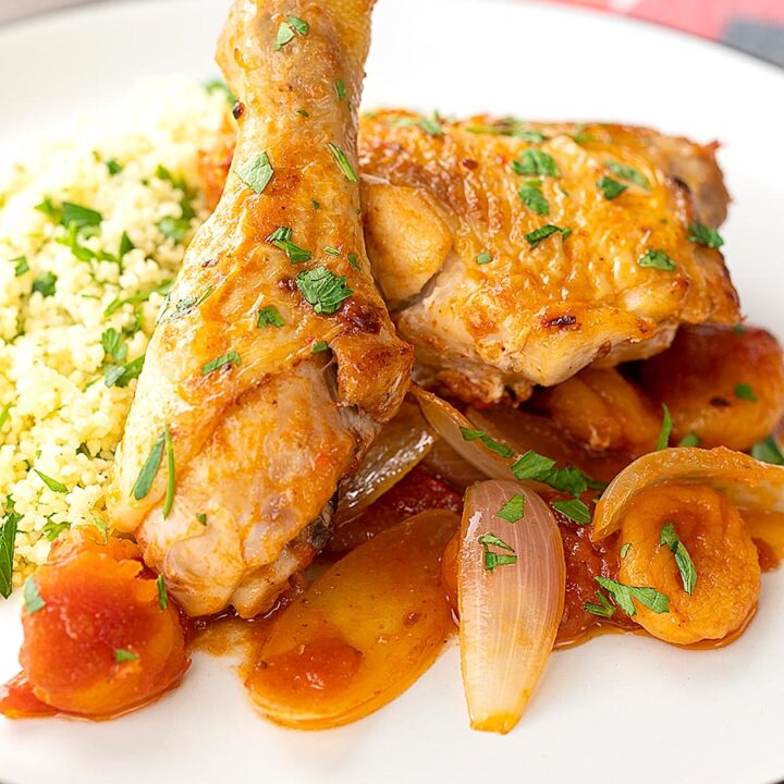 Portrait close up image of a Moroccan influenced chicken tagine with dried apricots made with chicken drumsticks and thighs served with buttered couscous