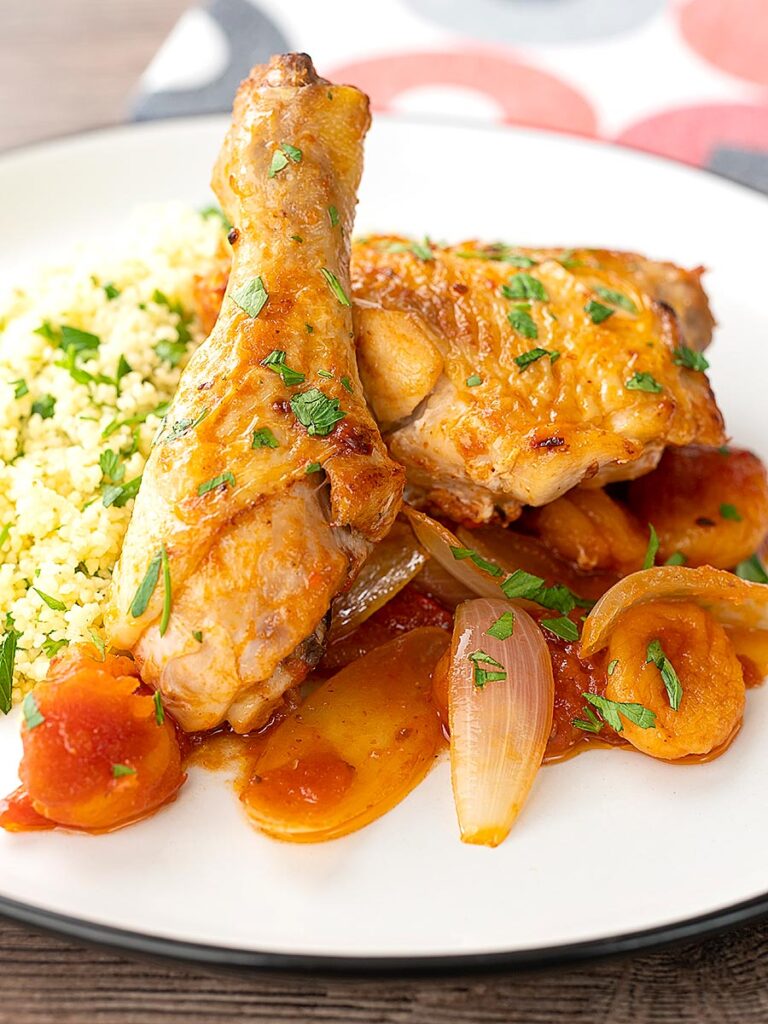 Portrait close up image of a Moroccan influenced chicken tagine with dried apricots made with chicken drumsticks and thighs served with buttered couscous