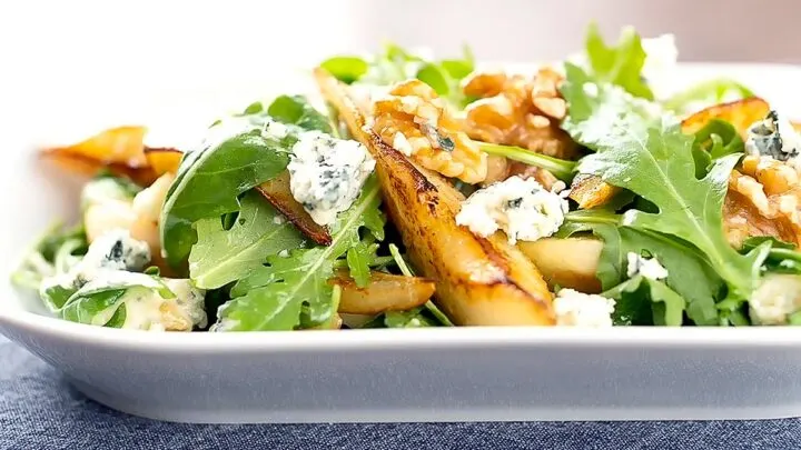 Landscape image of a pear and blue cheese salad with rocket (arugula) and walnuts served in a white bowl