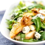 Portrait image of a pear and blue cheese salad with rocket (arugula) and walnuts served in a white bowl