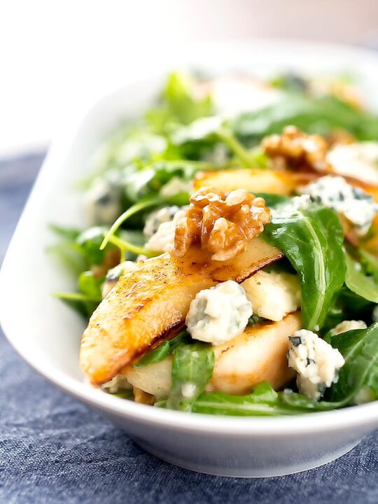 Portrait image of a pear and blue cheese salad with rocket (arugula) and walnuts served in a white bowl