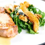 Portrait image of a pear and blue cheese salad with rocket (arugula) and walnuts served as a side dish to a pork chop