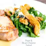 Portrait image of a pear and blue cheese salad with rocket (arugula) and walnuts served as a side dish to a pork chop with a text overlay