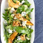 Portrait overhead image of a pear and blue cheese salad with rocket (arugula) and walnuts served in a white bowl