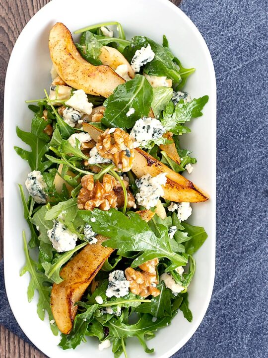 Portrait overhead image of a pear and blue cheese salad with rocket (arugula) and walnuts served in a white bowl