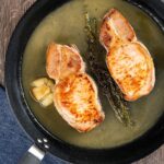 Portrait overhead image pork loin steaks in a cider sauce in a non stick skillet