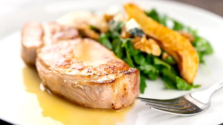 landscape image of a pork loin steak served on a white plate with a cider sauce and side salad