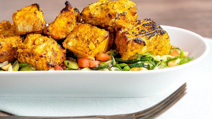 Landscape image of grilled salmon tikka served on a cucumber salad