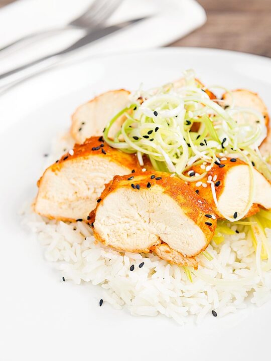 Portrait image of a sliced steamed chicken breast cooked in a spicy Korean gochujang marinade served on white rice