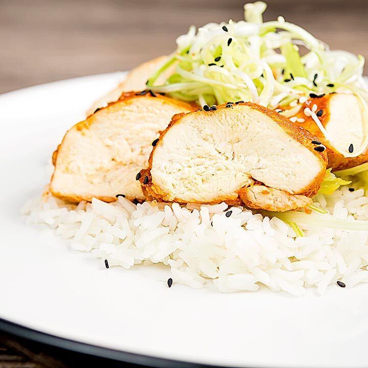 Square image of a sliced steamed chicken breast cooked in a spicy Korean gochujang marinade served on white rice