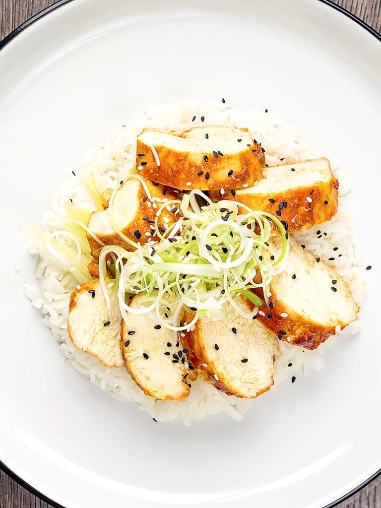 Portrait overhead image of a sliced steamed chicken breast cooked in a spicy Korean gochujang marinade served on white rice