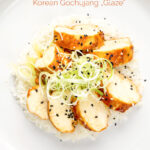 Portrait overhead image of a sliced steamed chicken breast cooked in a spicy Korean gochujang marinade served on white rice with a text overlay