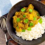 Portrait overhead image of a Burmese influenced vegan pumpkin curry served with white rice and fresh coriander