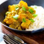 Portrait image of a Burmese influenced vegan pumpkin curry served with white rice and fresh coriander