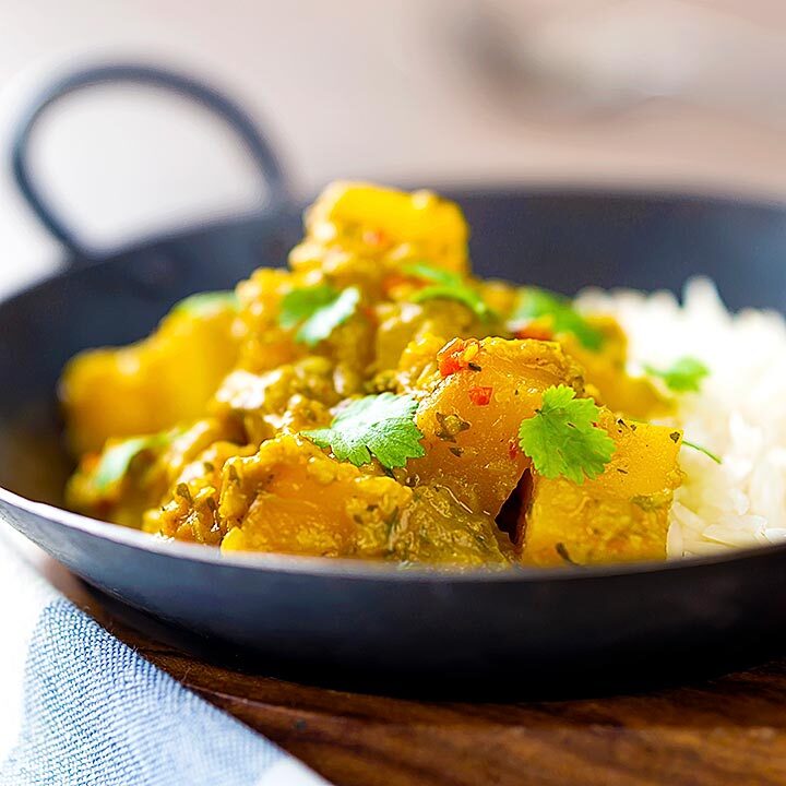 Square image of a Burmese influenced vegan pumpkin curry served with white rice and fresh coriander