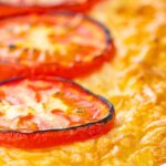 Portrait close up image of cheese and potato pie bake topped with tomato slices