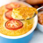 Portrait close up image of cheese and potato pie bake topped with tomato slices with a spoon taking out a piece with a text overlay