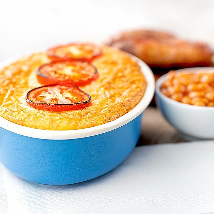 Square image of cheese and potato pie bake served with sausages and baked beans