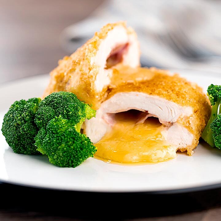 Square image of chicken cordon bleu, cheese and ham stuffed chicken breast served with broccoli cut open to show oozing cheese
