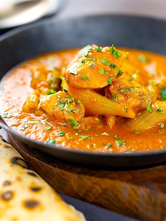 Portrait image of a chicken jalfrezi curry with a coriander garnish served in an iron karahi bowl and chapatis