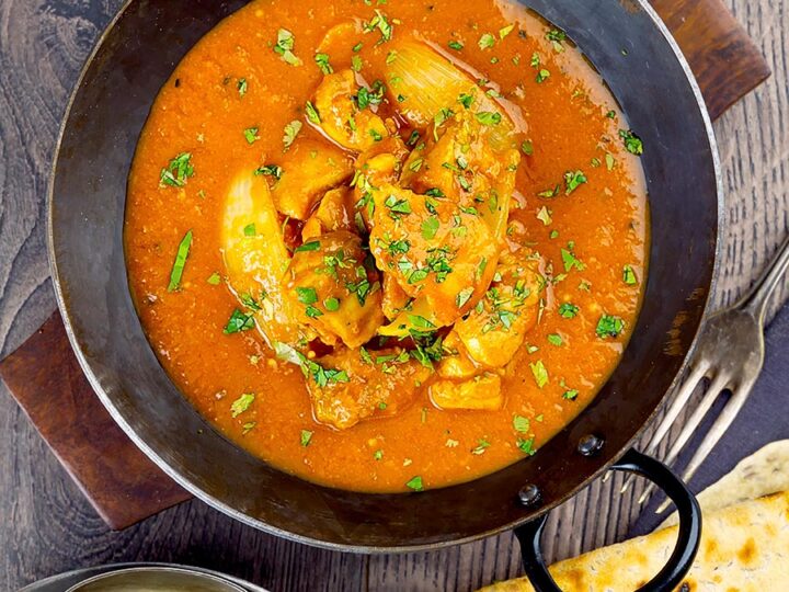 Portrait overhead image of a chicken jalfrezi curry with a coriander garnish served in an iron karahi bowl and chapatis and boiled rice