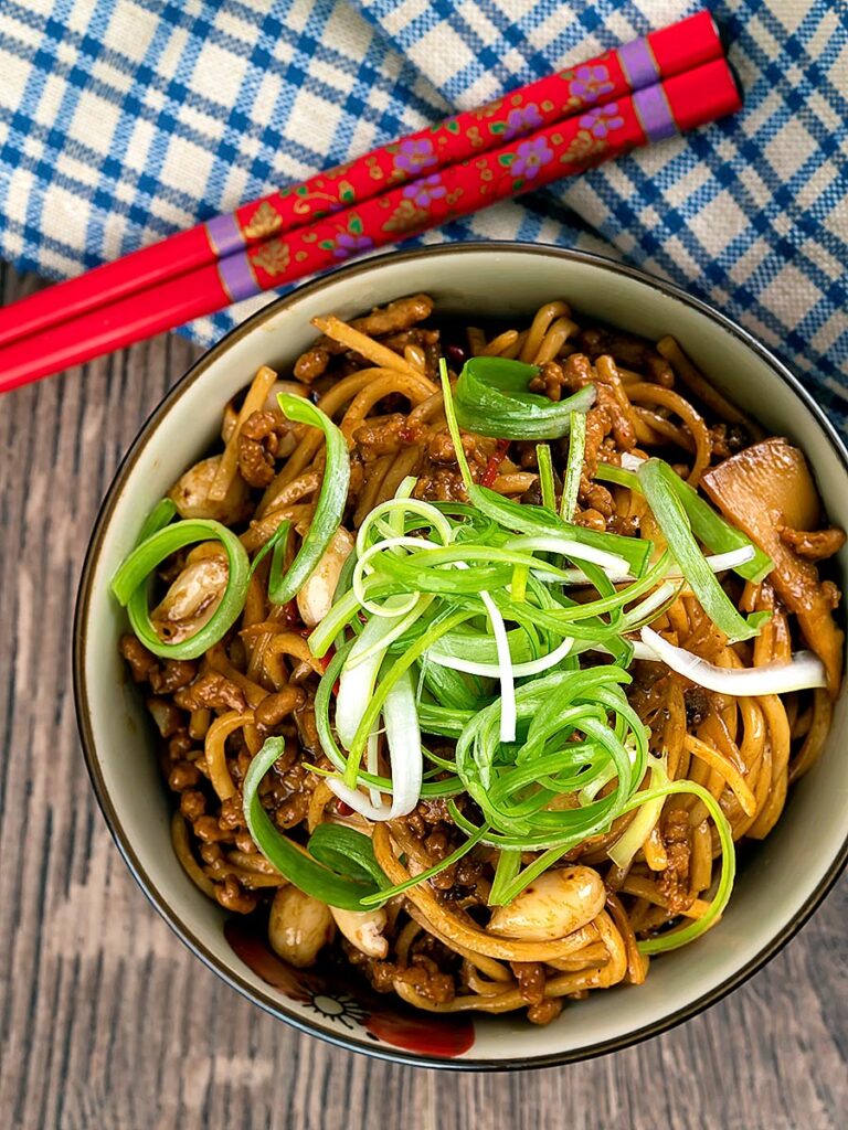 Portrait overhead image of dan dan noodles, a Chinese stir fried minced pork recipe served with a spring onion garnish